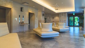 A modern lobby with a reception desk, seating area, and a view of the outdoors. - Hotel Sunset Hill (Onna)
