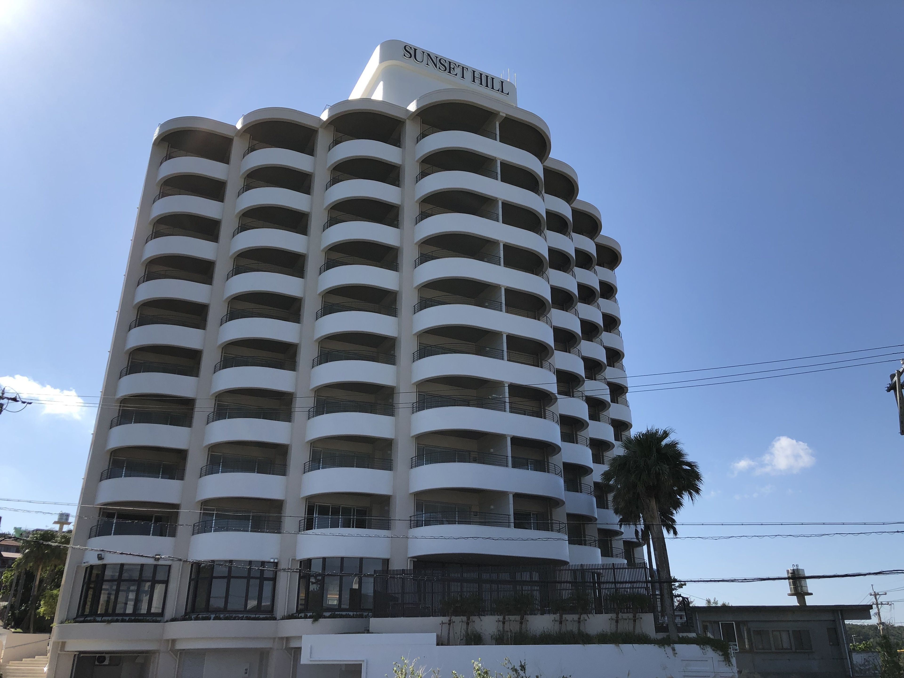 Et hotel med flere etager, en buet facade og altaner på hver etage, med et skilt der viser "SUNSET HILL".