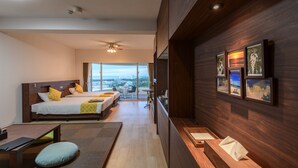 A modern hotel room with a large bed, a desk, and a view of the city. - Hotel Sunset Hill (Onna)