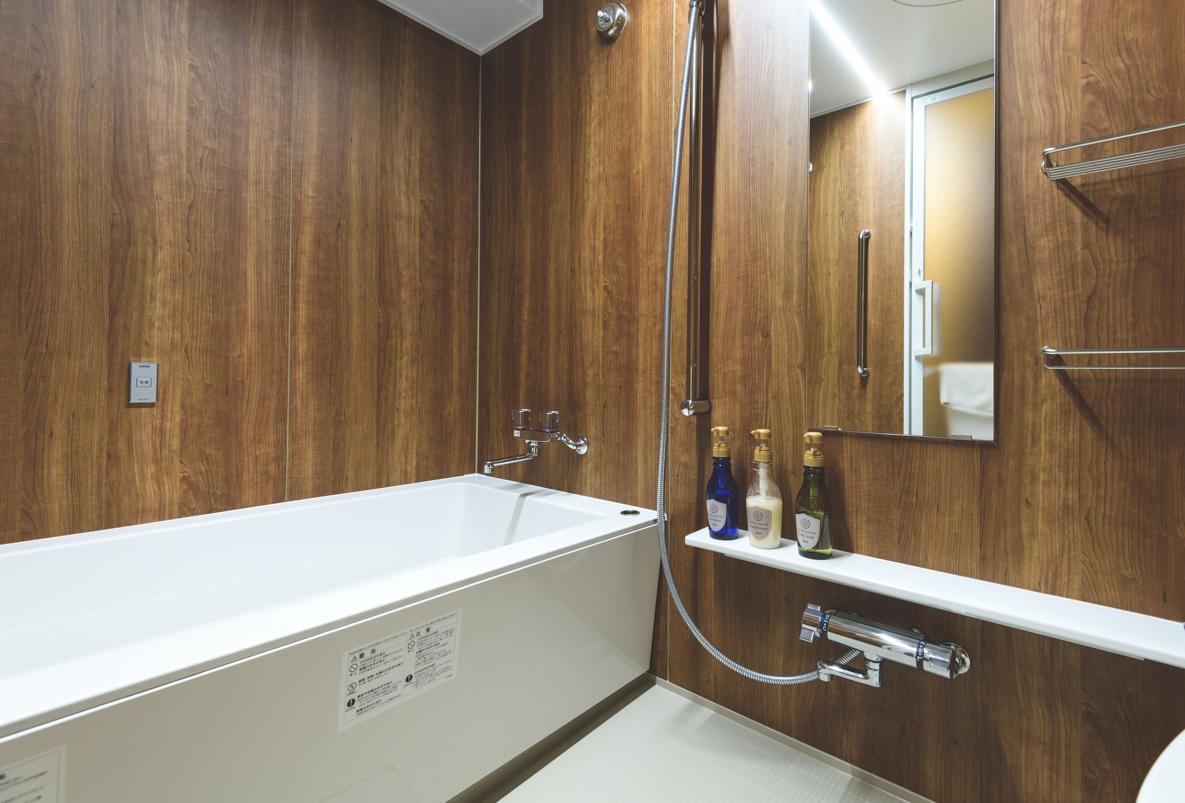 A modern bathroom with a wooden wall, a white bathtub, and a built-in shelf with toiletries.
