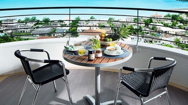 A balcony with a table set for two, overlooking a coastal view. - Hotel Sunset Hill (Onna)