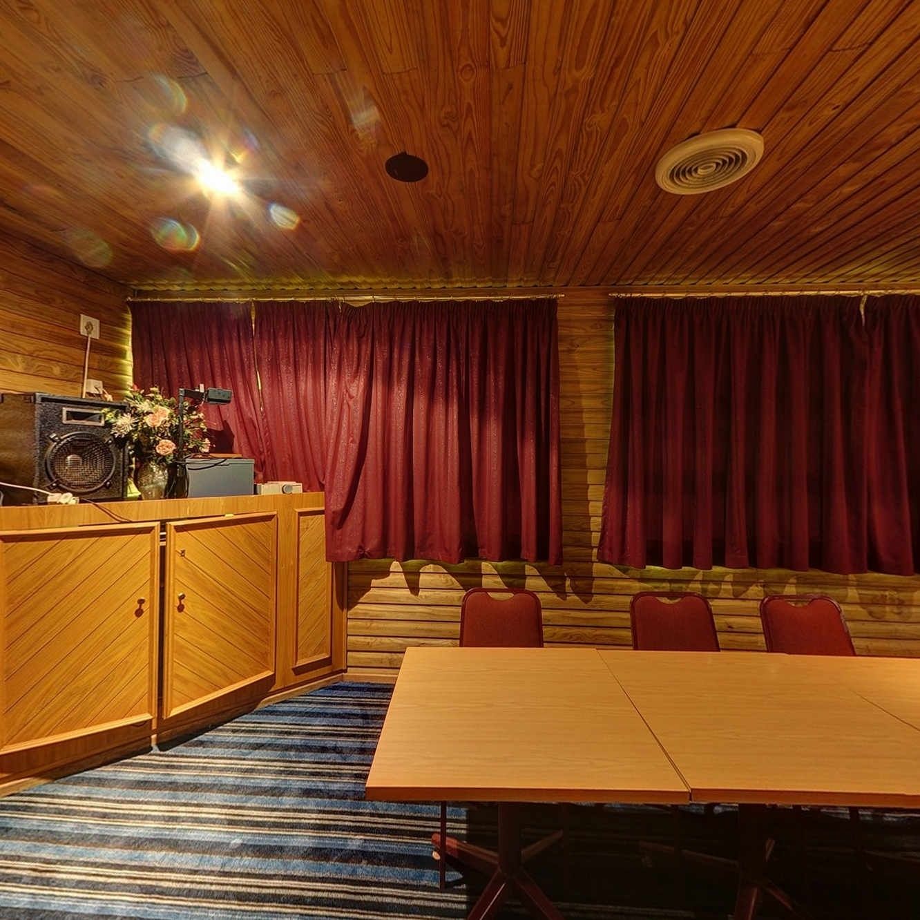 Une pièce aux murs lambrés, avec une grande table, des rideaux rouges et un haut-parleur.