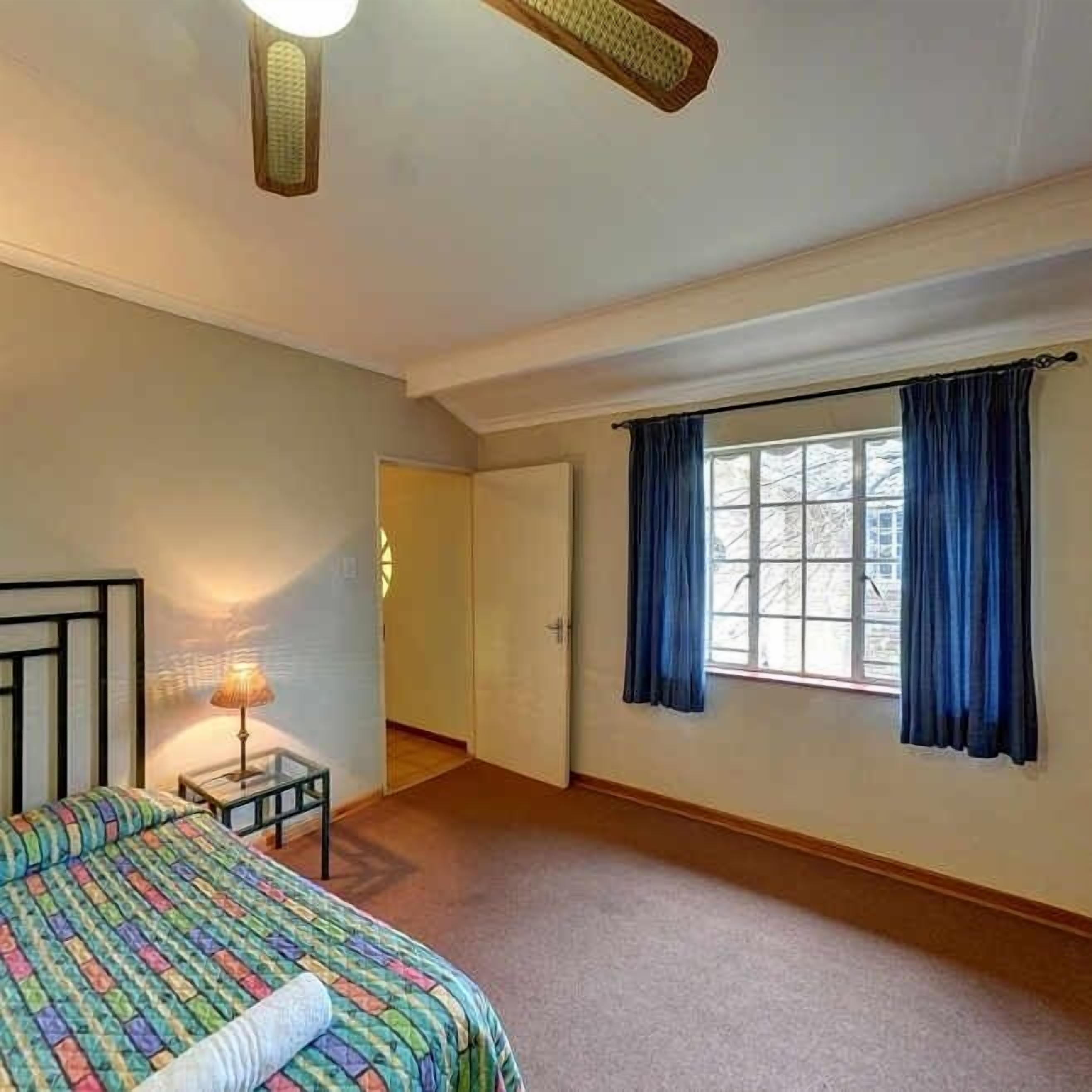 Ein Schlafzimmer mit einem Bett, einem Nachttisch, einem Fenster mit Vorhängen und einer Tür zu einem anderen Raum.