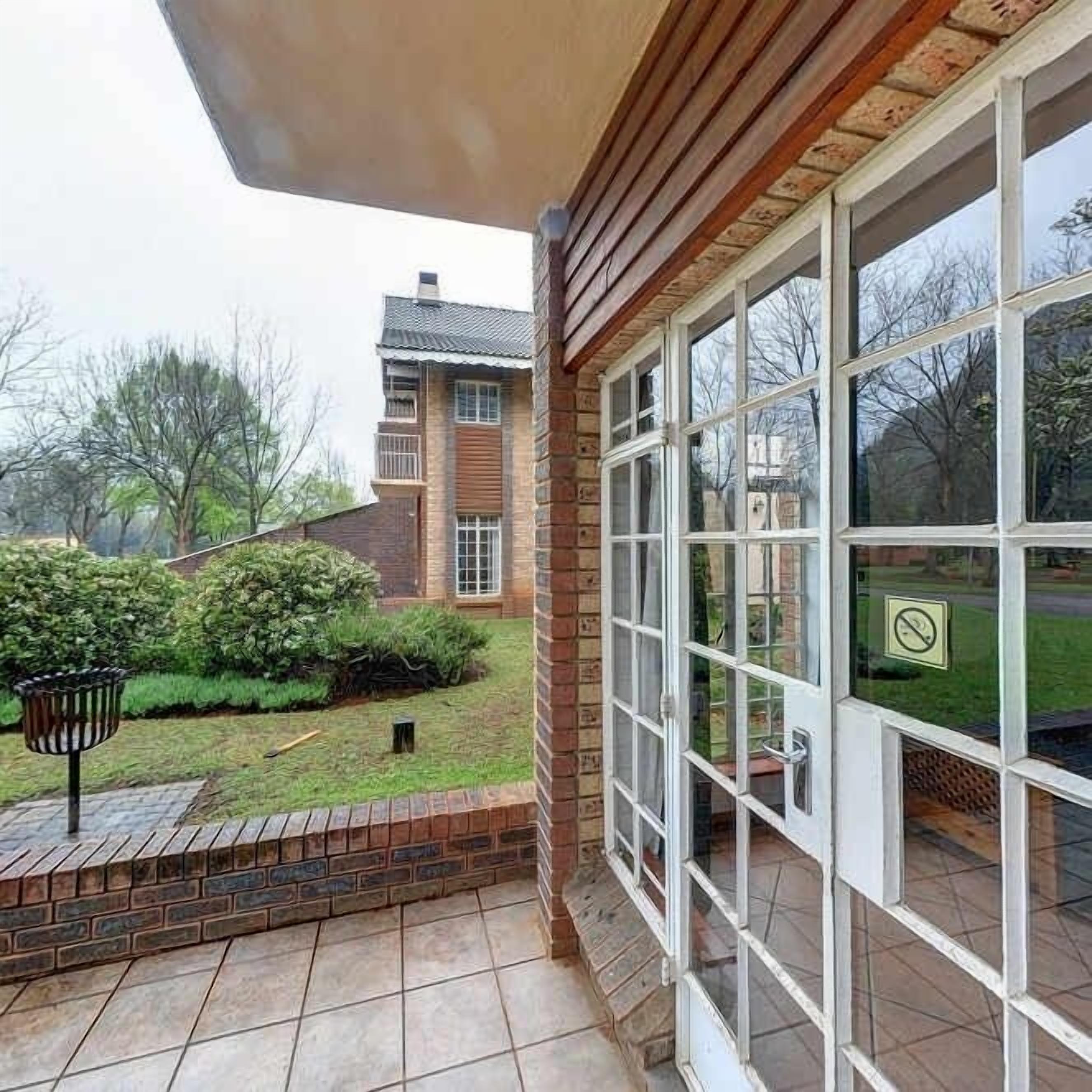 A covered patio with a view of a brick house and garden.