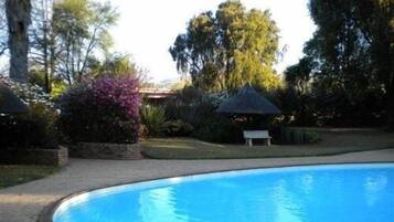 A swimming pool with a curved edge, surrounded by a paved area and various trees and shrubs.