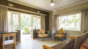 Una habitación con pared de ladrillo, muebles de madera y ventanas amplias con cortinas.