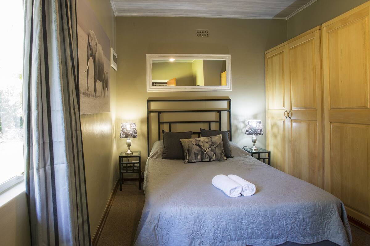 A neatly made bed with a rolled towel, a mirror above it, and two bedside tables with lamps.