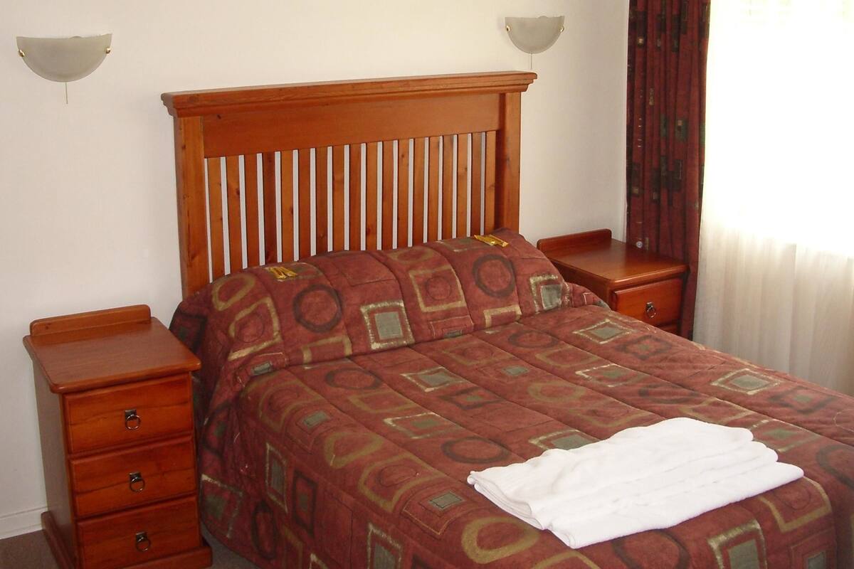 A neatly made bed with a patterned bedspread, two bedside tables, and wall-mounted lamps.