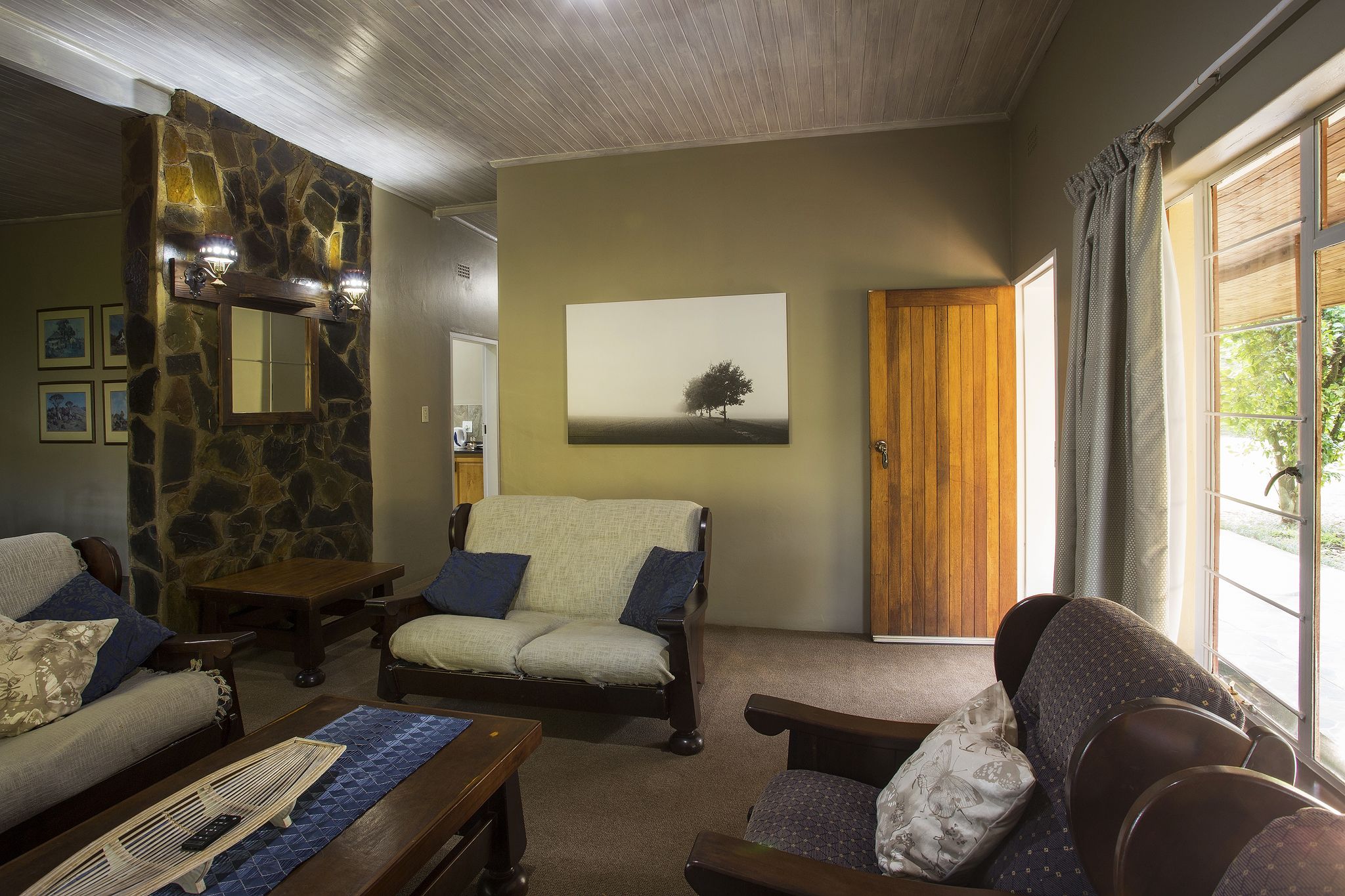 Una sala de estar acogedora con una pared de piedra decorativa, un cuadro grande y vistas a través de una ventana.