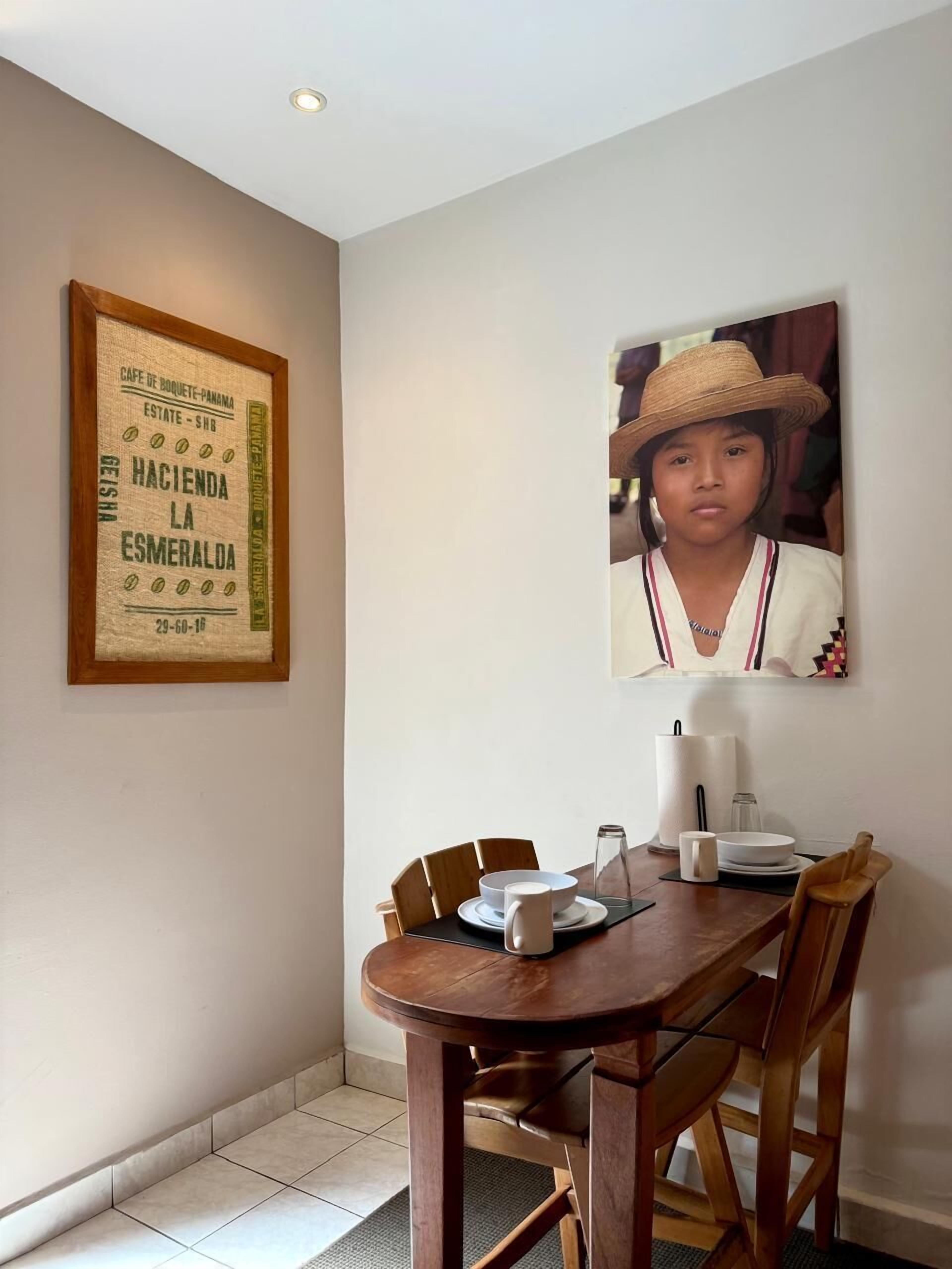 Un comedor con una mesa de madera dispuesta para dos personas, un cartel antiguo enmarco y una fotografía colgada en la pared.