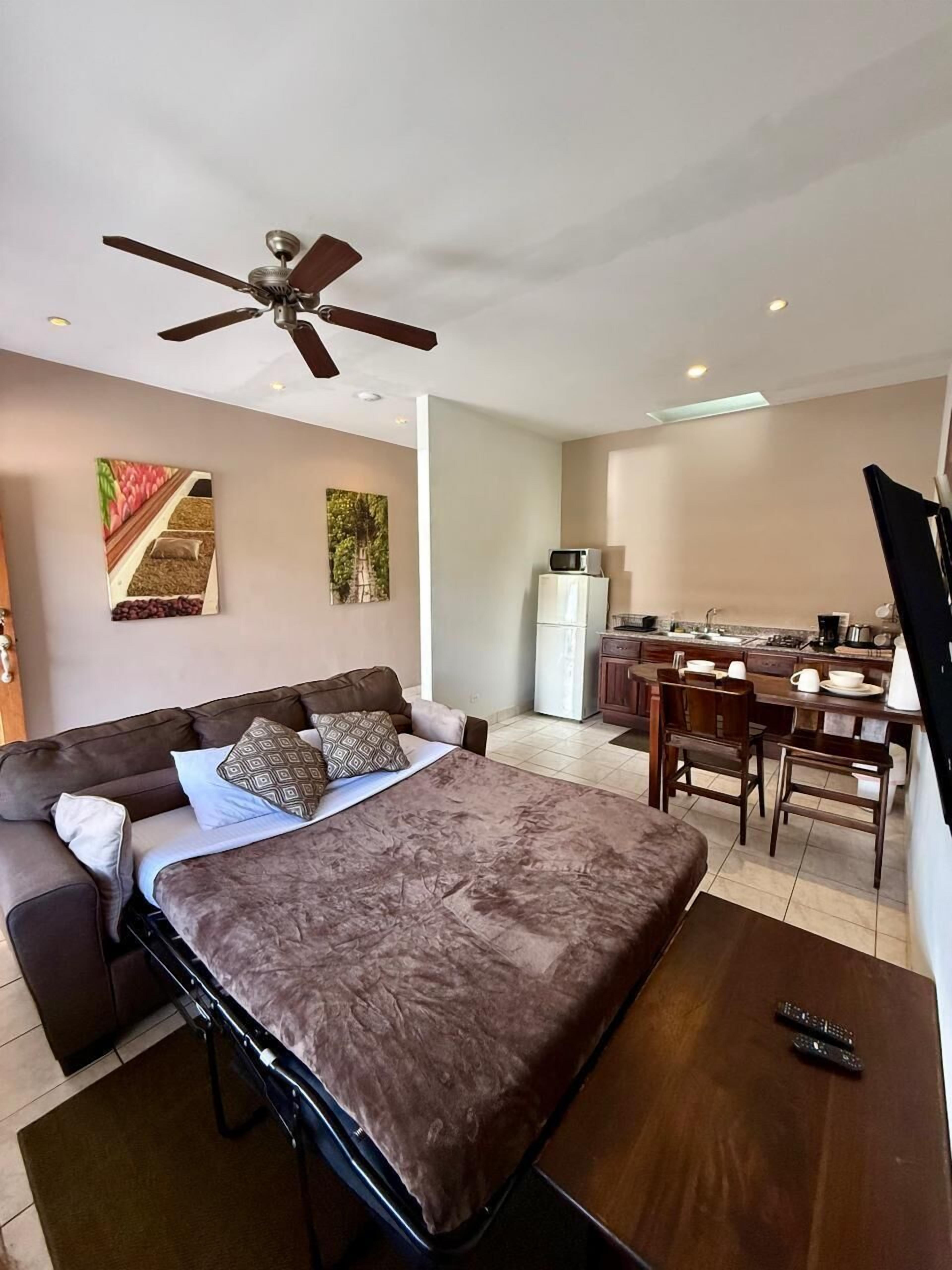 A modern hotel room with a bed, a desk, and a kitchenette.