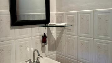 Bagno con lavandino bianco, specchio con cornice nera e dispenser di sapone su ripiano in vetro.