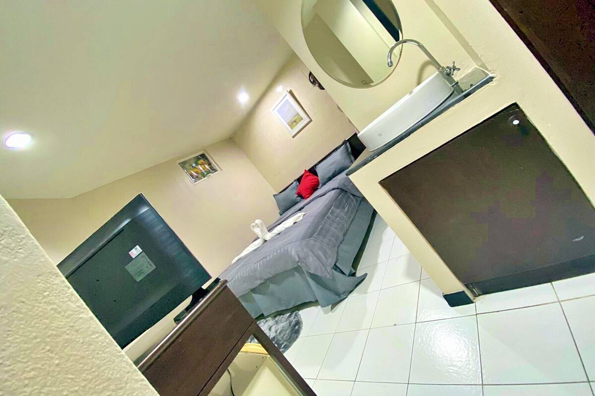 A hotel room with a bed, a bedside table, a mirror, a window, and a television.