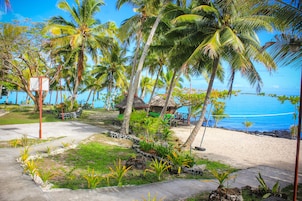 Un resort frente a la playa con palmeras, una cabaña de techo de paja y vistas despejadas del océano.