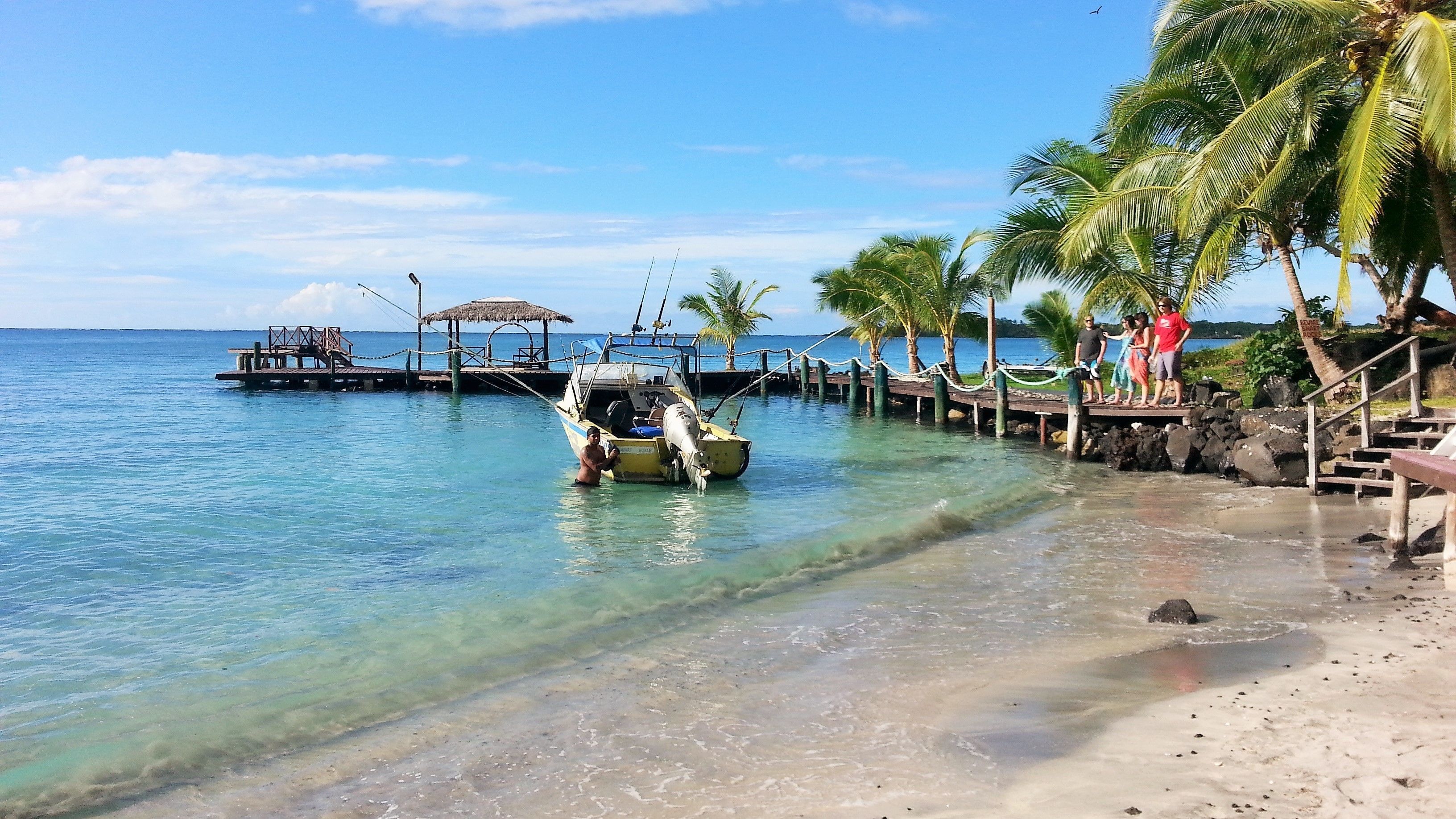 A beach with clear water, a dock, and a small boat.