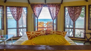 A room with a bed, a table, and a view of the sea through curtains. - Va-i-moana Seaside Lodge (Asau)