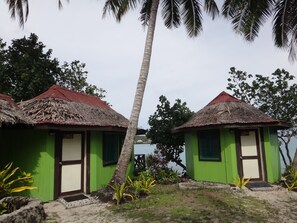 Two green-roofed cottages with thatched roofs, surrounded by palm trees and vegetation. - Va-i-moana Seaside Lodge (Asau)