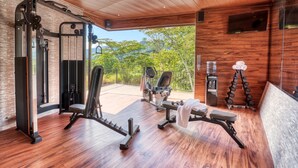Ein modernes Fitnessstudio mit Holzboden und Geräten, große Fenster mit Blick auf Grünflächen.
