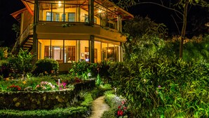 Ein zweigeschossiges Haus mit Balkon, umgeben von üppiger Bepflanzung und einem Gartenweg.