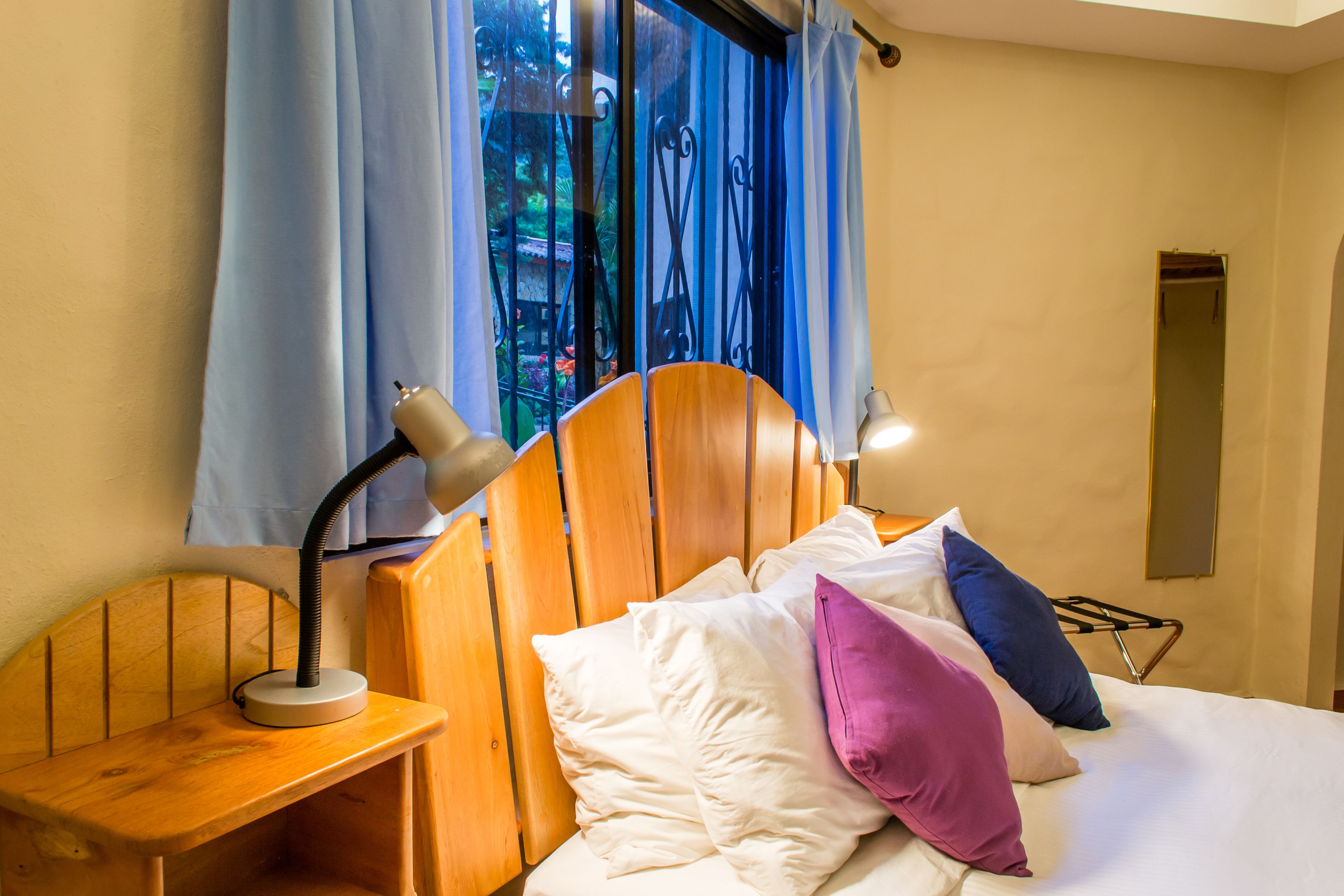 A neatly made bed with white and purple pillows, a wooden headboard, and a bedside table with a lamp.