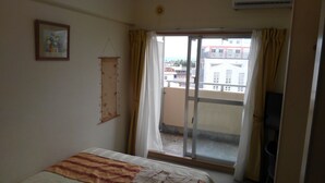 A bedroom with a bed, a window with curtains, a wall-mounted air conditioning unit, and a framed picture.
