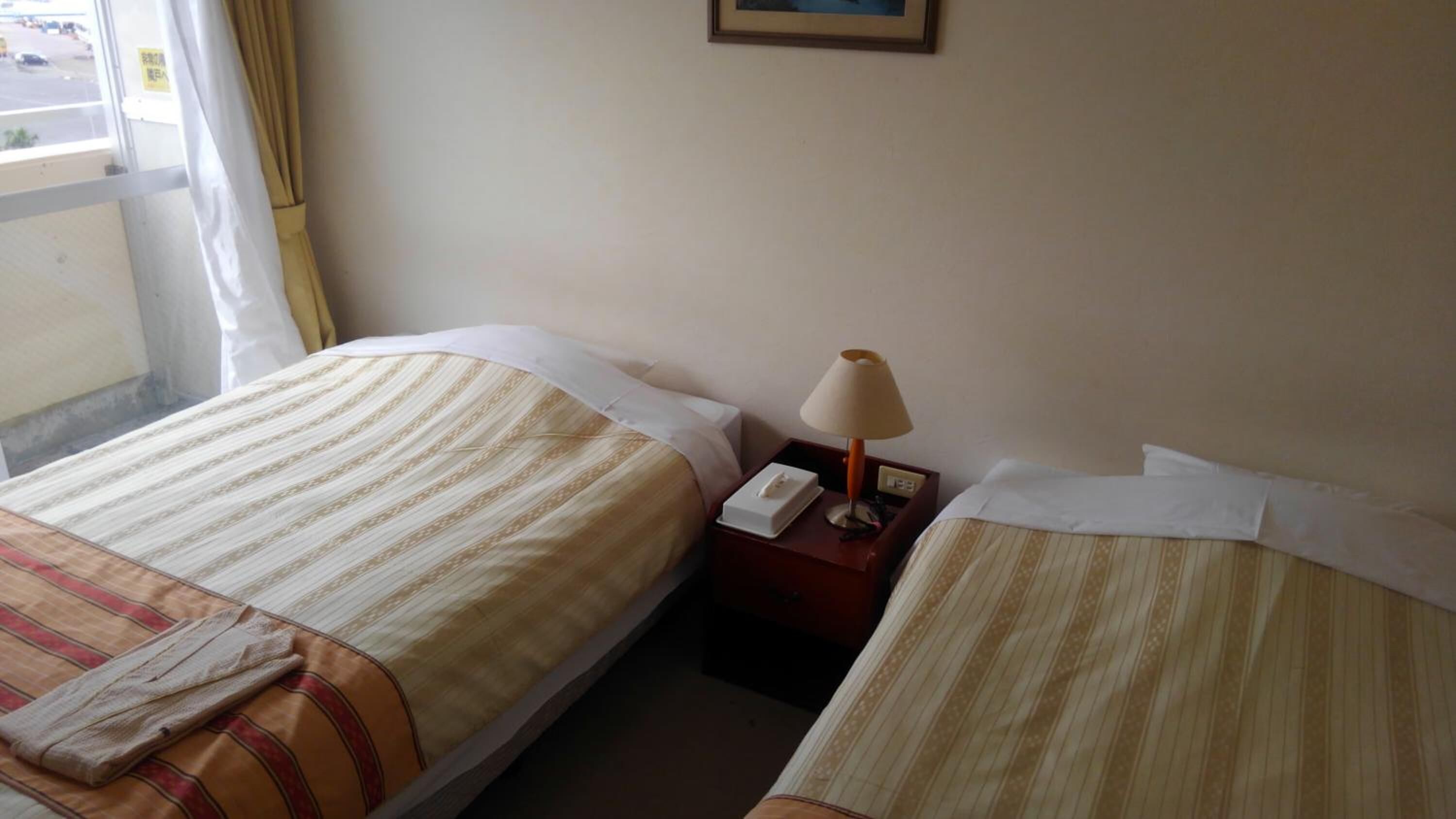 Ein Hotelzimmer mit zwei Betten, einem Nachttisch mit Lampe und einem Fenster mit Vorhängen.