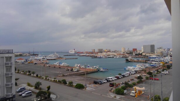 A marina with boats, a large cruise ship, and a cityscape in the background.