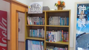 A bookshelf with various books, a sign with Japanese text, and a framed picture of a resort.