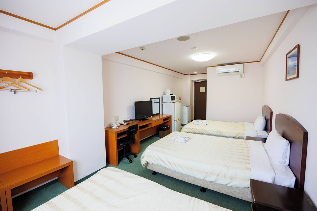 Ein Hotelzimmer mit zwei Betten, einem Schreibtisch mit Computer, einem Sessel und einem kleinen Tisch.