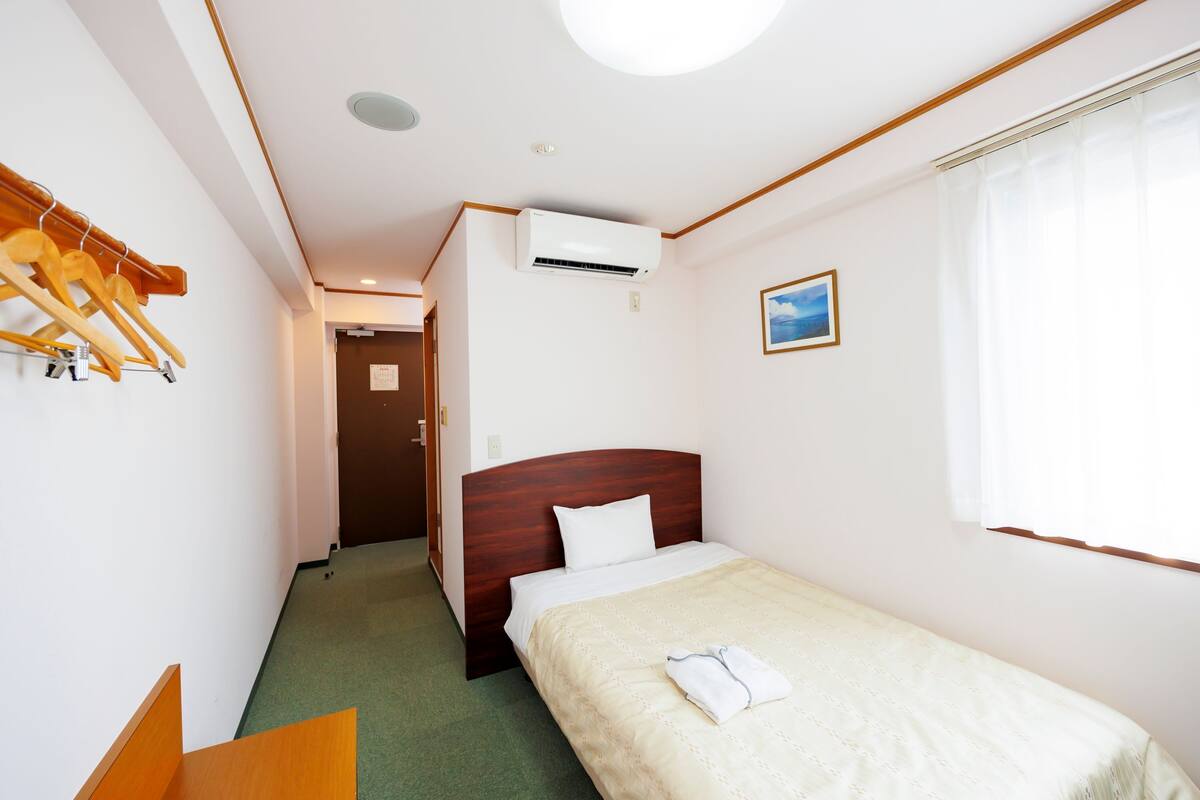 Ein Hotelzimmer mit einem Bett, einem Holzkopfteil, einer Klimaanlage, einem Fenster mit Vorhängen und einem Wandbild.