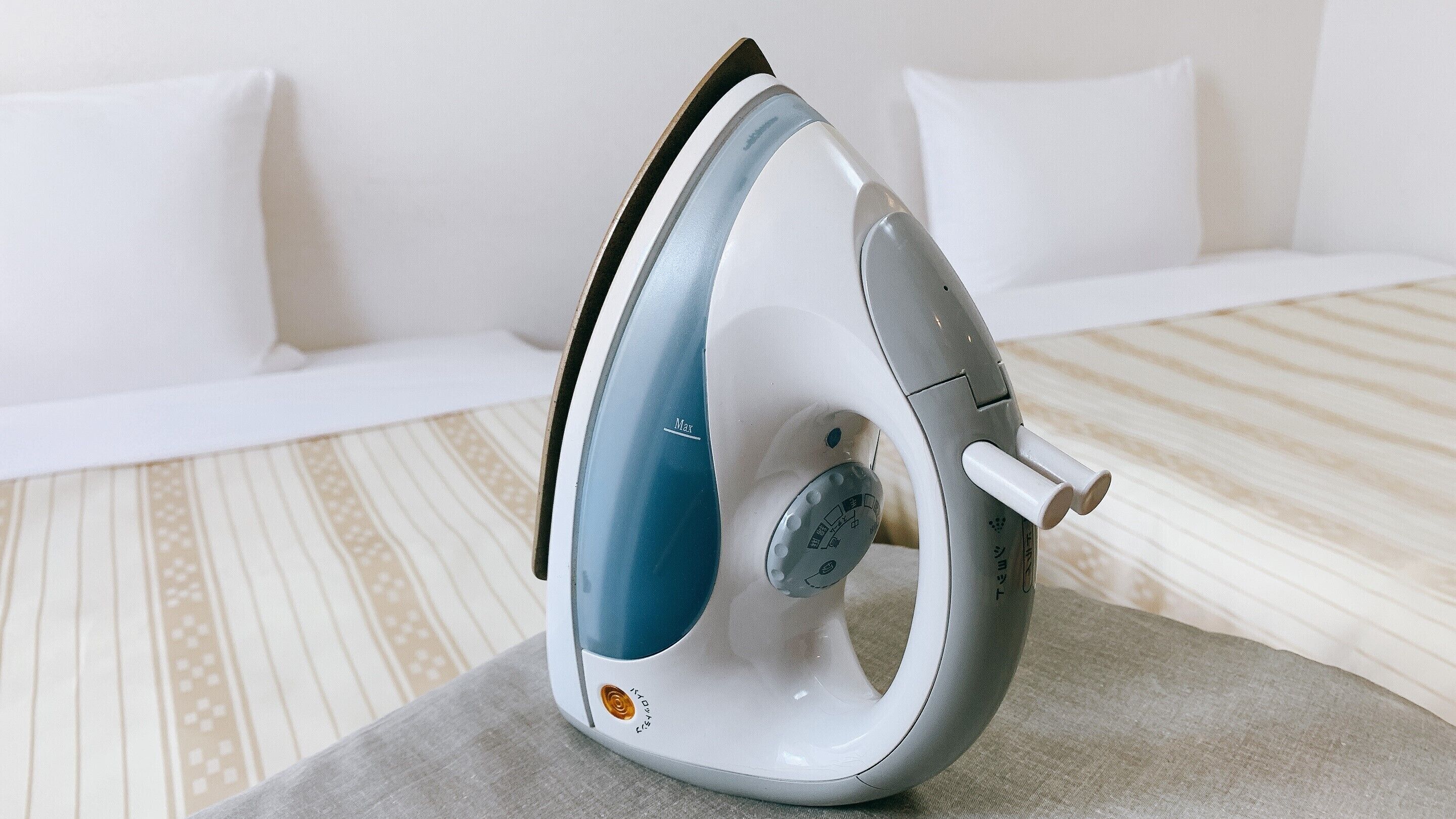 A modern, compact iron with a blue and white color scheme, placed on a grey surface in a room with a striped carpet and white furniture.
