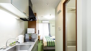 Una habitación de hotel compacta con kitchenette, una cama, ducha y baño pequeño.