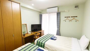 Habitación de hotel con dos camas, un escritorio con televisor, un armario y una ventana con cortinas.