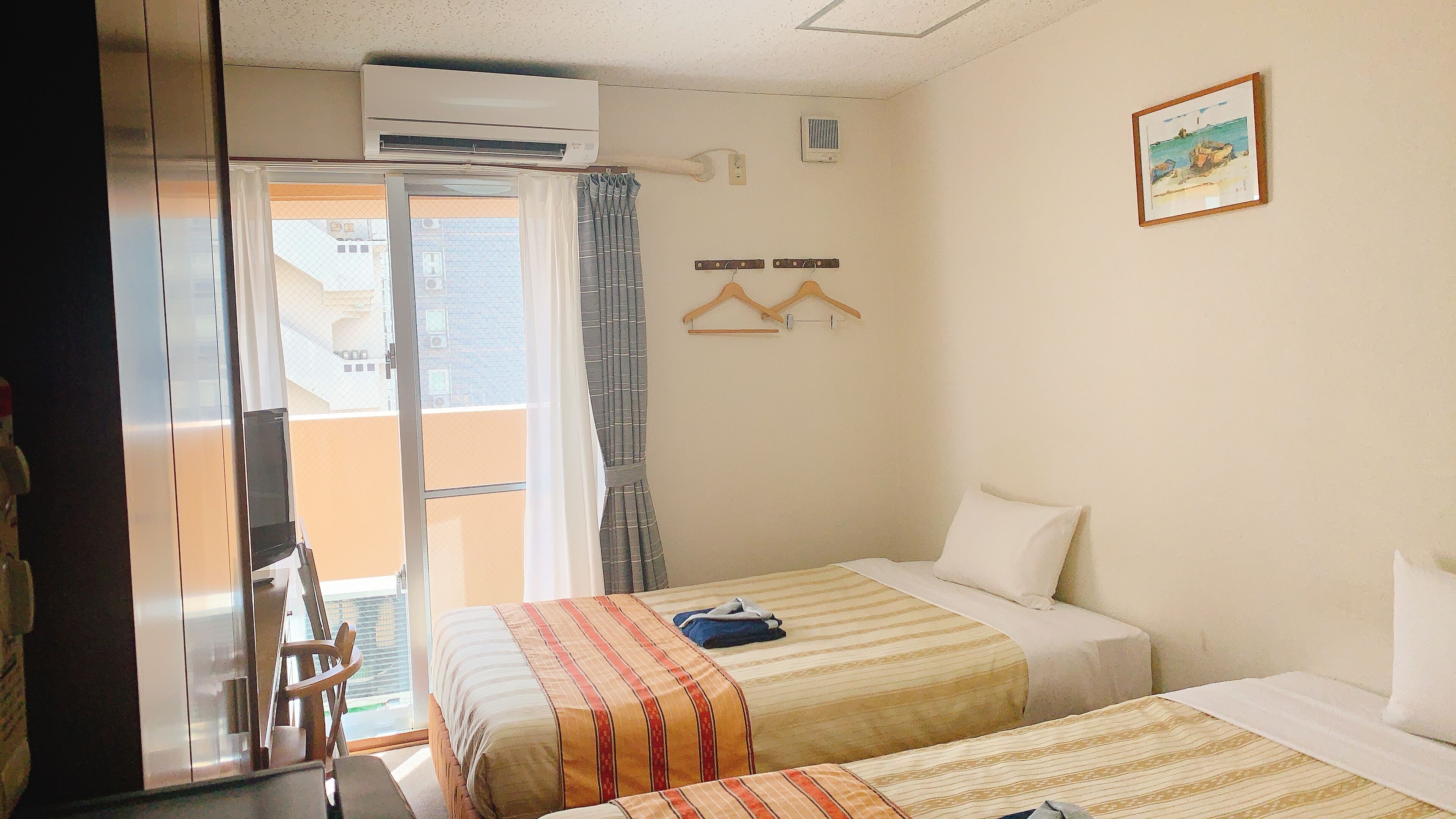 Une chambre d’hôtel avec deux lits, un balcon, un climatiseur, un radiateur mural et un tableau.