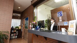 Un área de recepción con mostrador, un monitor de computadora, una planta y una estantería.