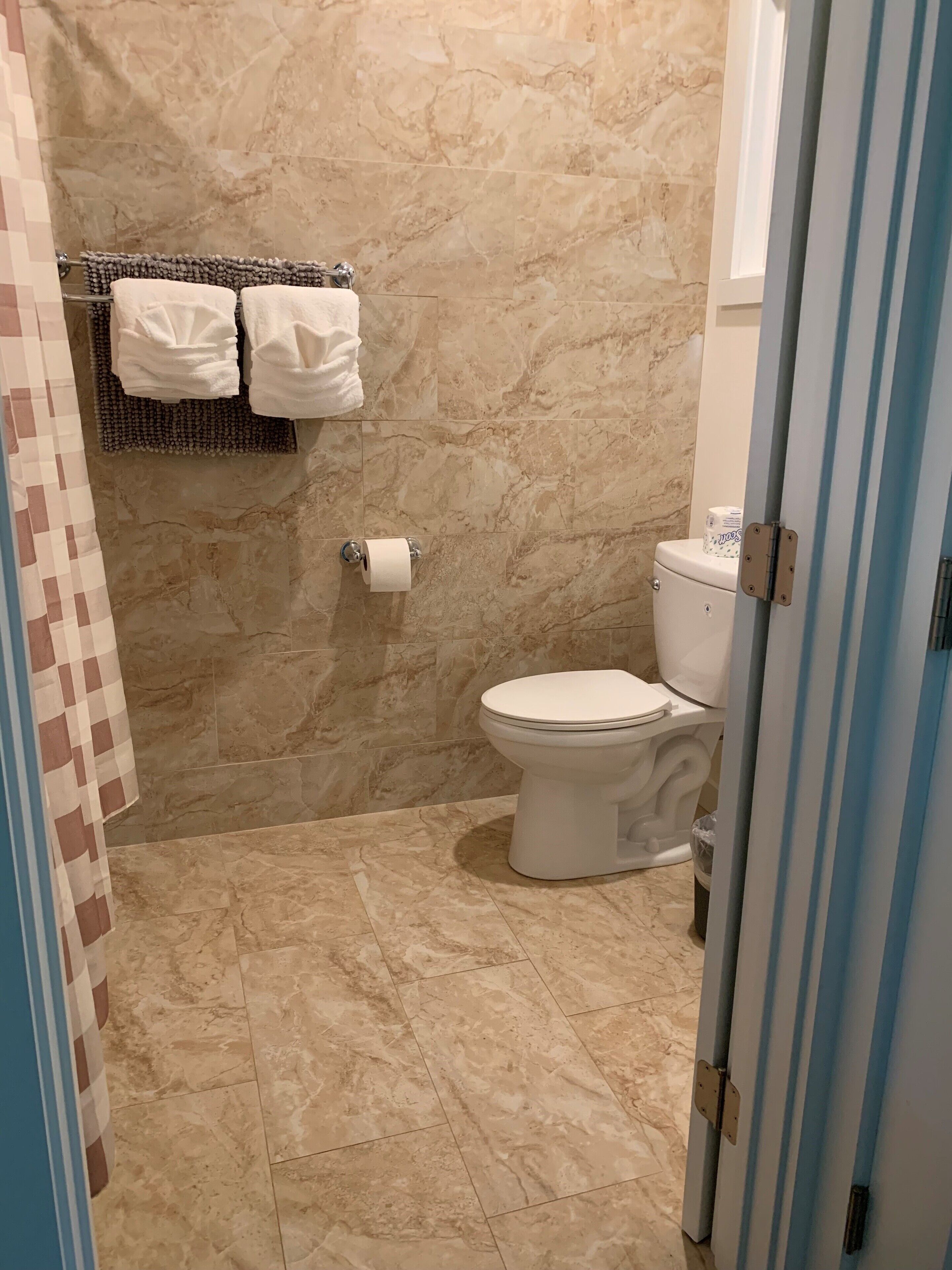 A bathroom with a toilet, marble walls, and a towel rack with two white towels.