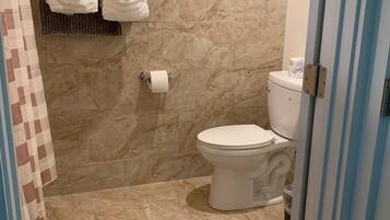 A bathroom with a toilet, marble walls, and a towel rack with two white towels.