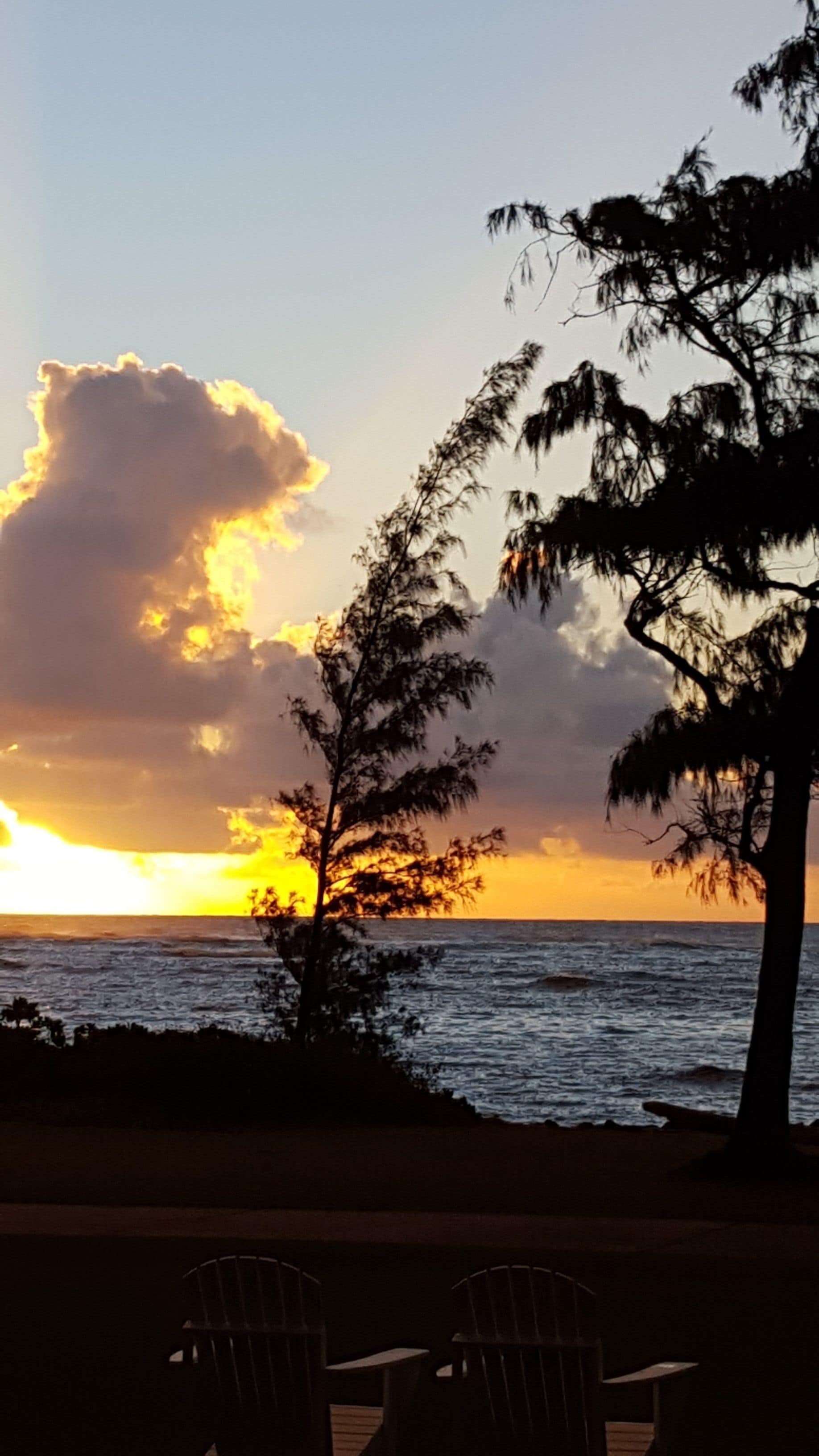 Vista al atardecer con playa y dos sillas al frente.