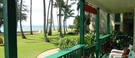 A covered porch with green railings overlooking a beach with palm trees and a view of the ocean.