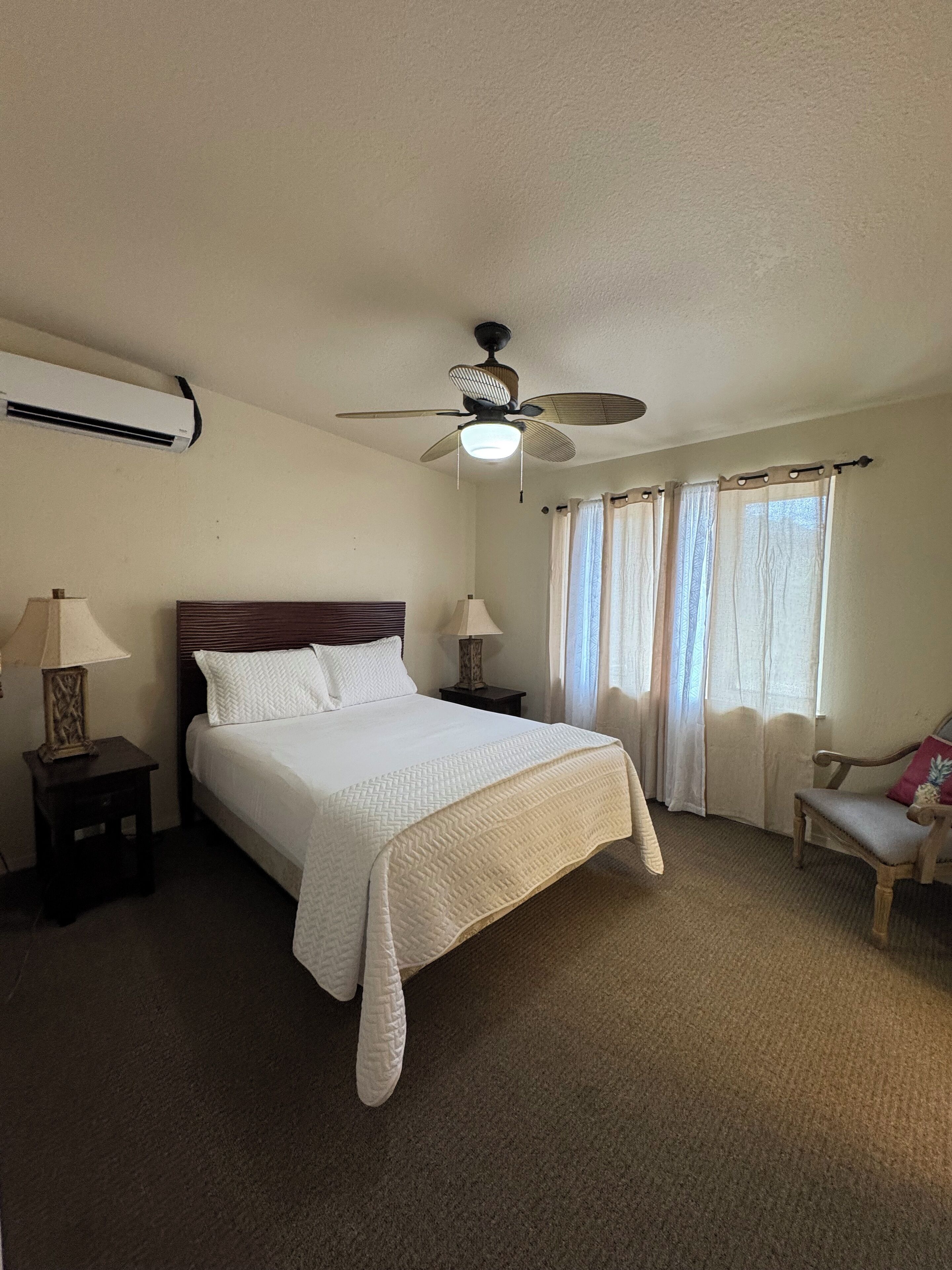 A neatly arranged bedroom with a bed, two bedside tables, a ceiling fan, and a window with curtains.