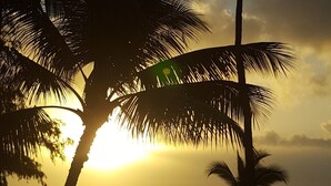 A sunset over the ocean with palm trees silhouetted against the sky. - Hotel Coral Reef (Kapaa)