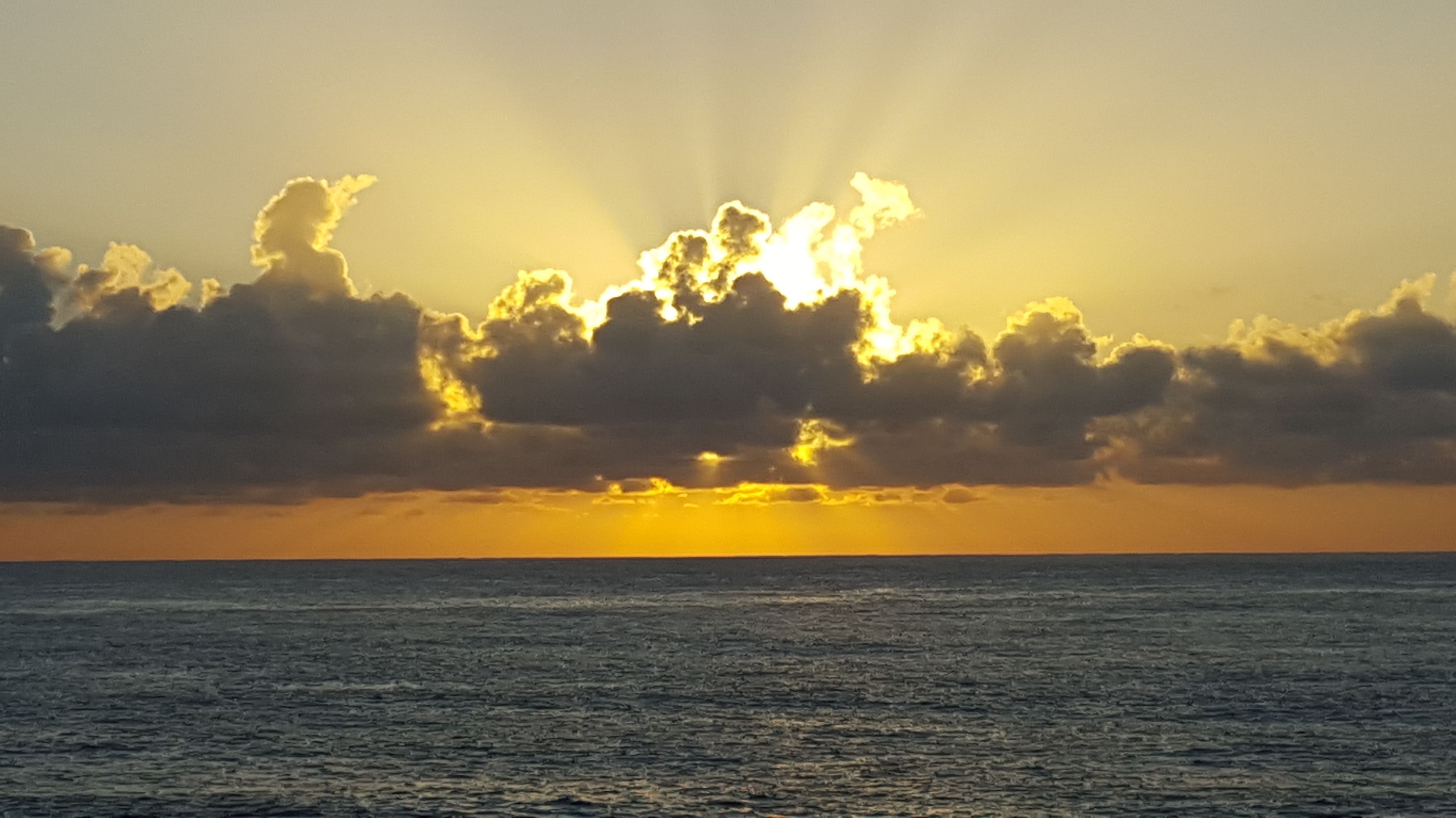A sunset over the ocean with clouds and sunlight.