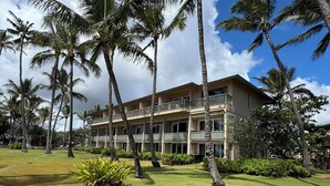 A multi-story hotel with balconies, surrounded by palm trees and well-maintained lawns. - Hotel Coral Reef (Kapaa)