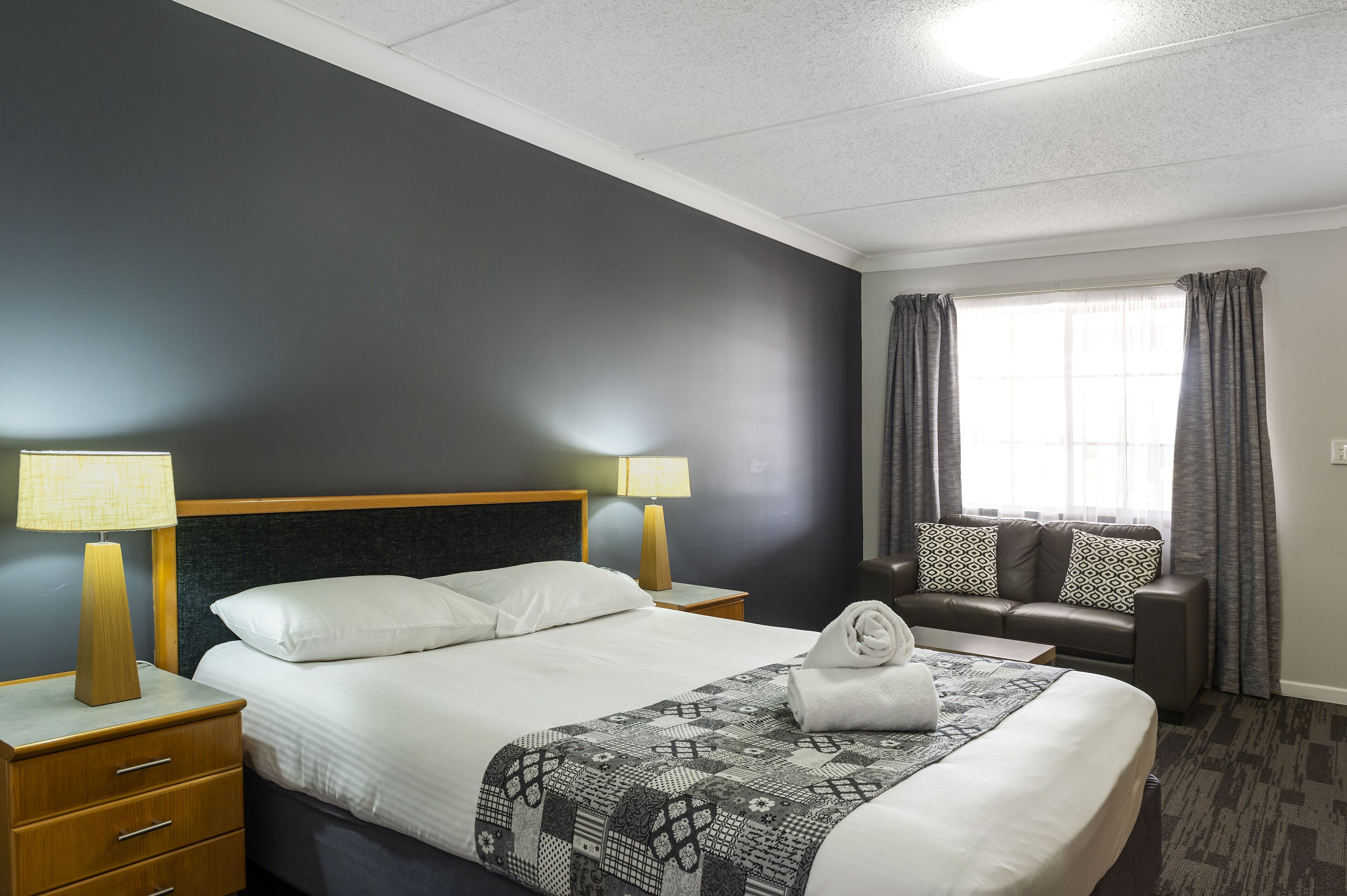 Een hotelkamer met een bed, twee bedlampen, een bank en een raam met gordijnen.