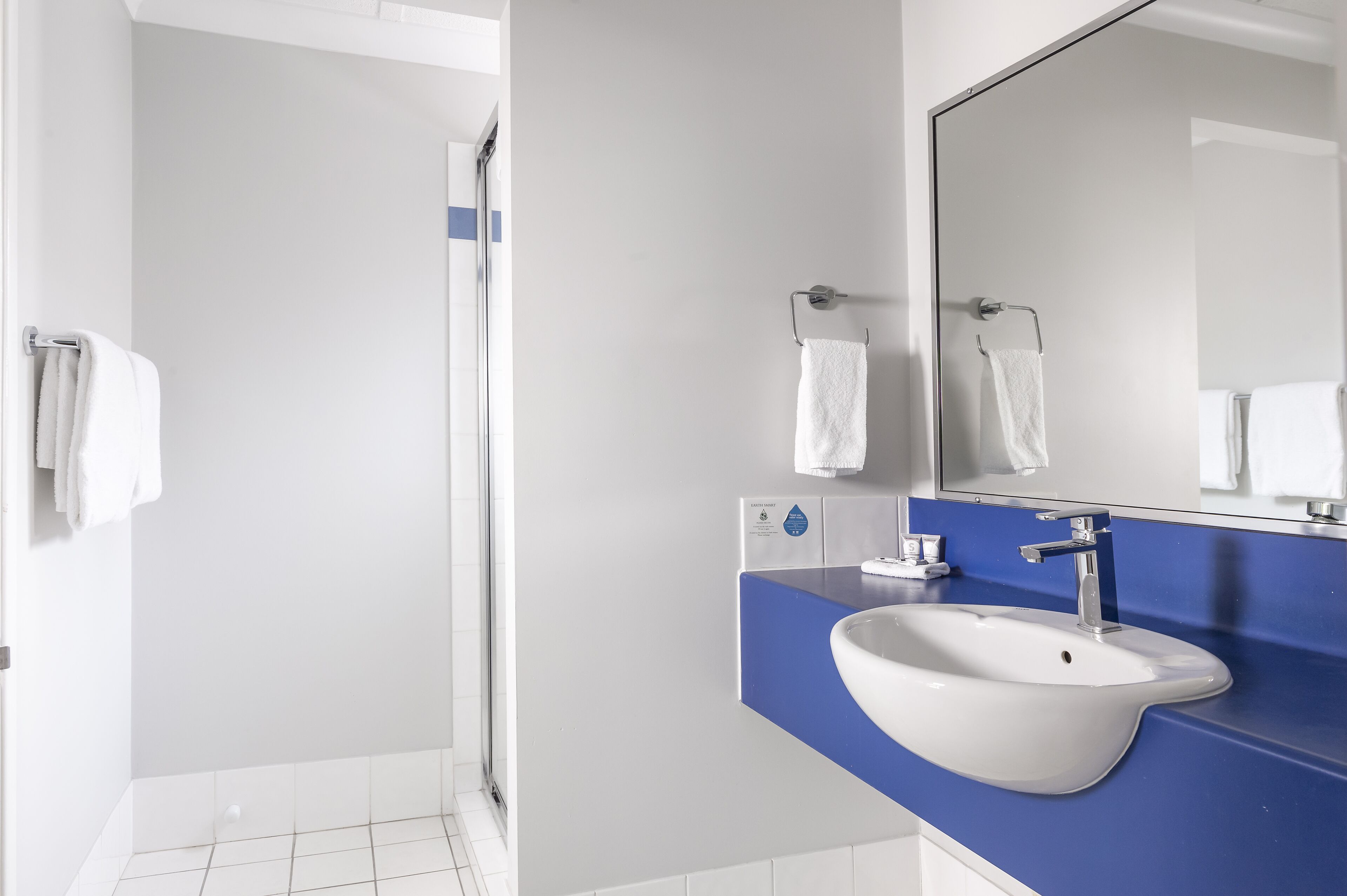 Une salle de bain moderne avec un lavabo blanc, un plan de toilette bleu et un grand miroir.