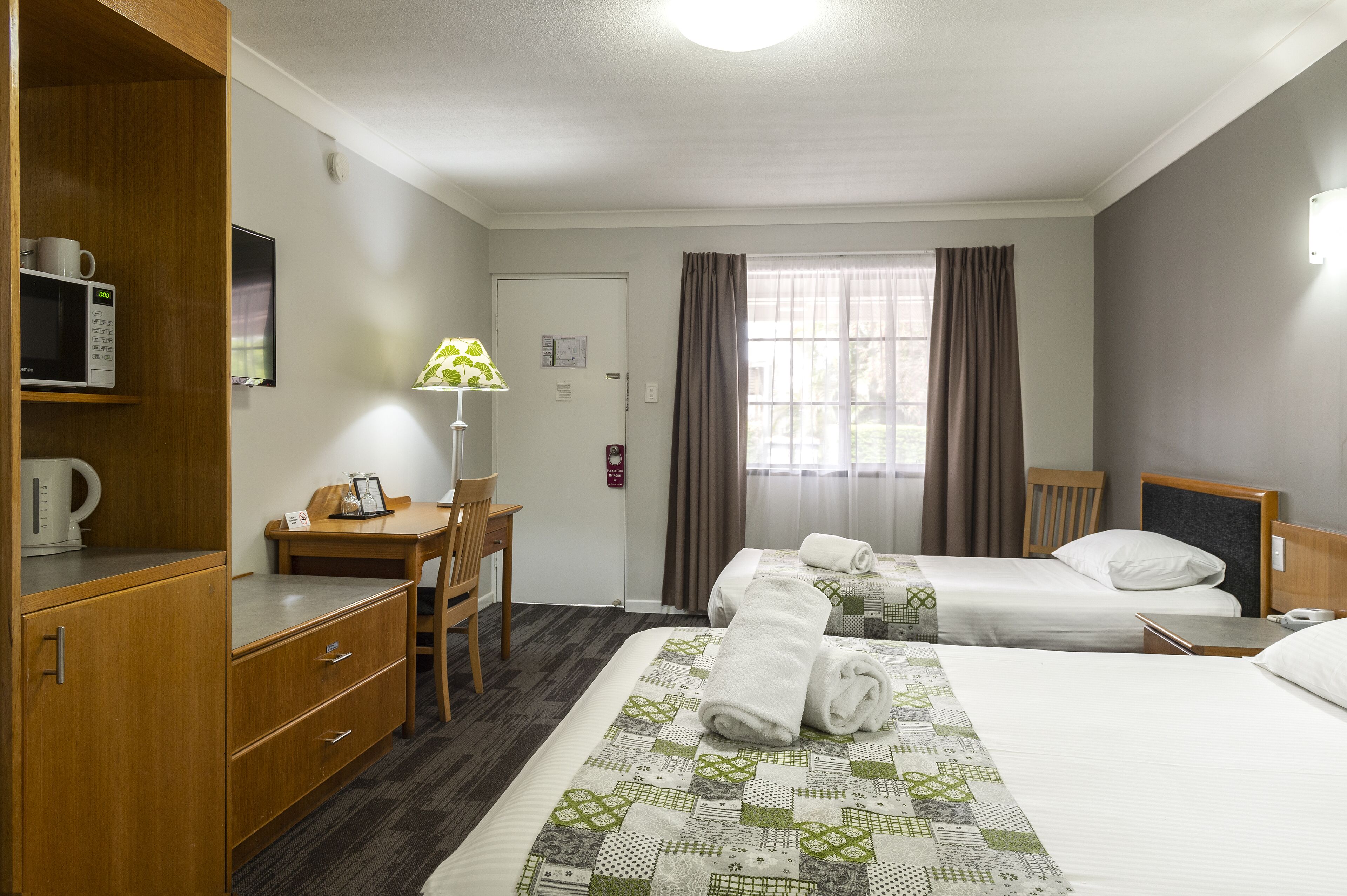 Habitación de hotel con dos camas, un escritorio, una silla, un microondas y una lámpara.