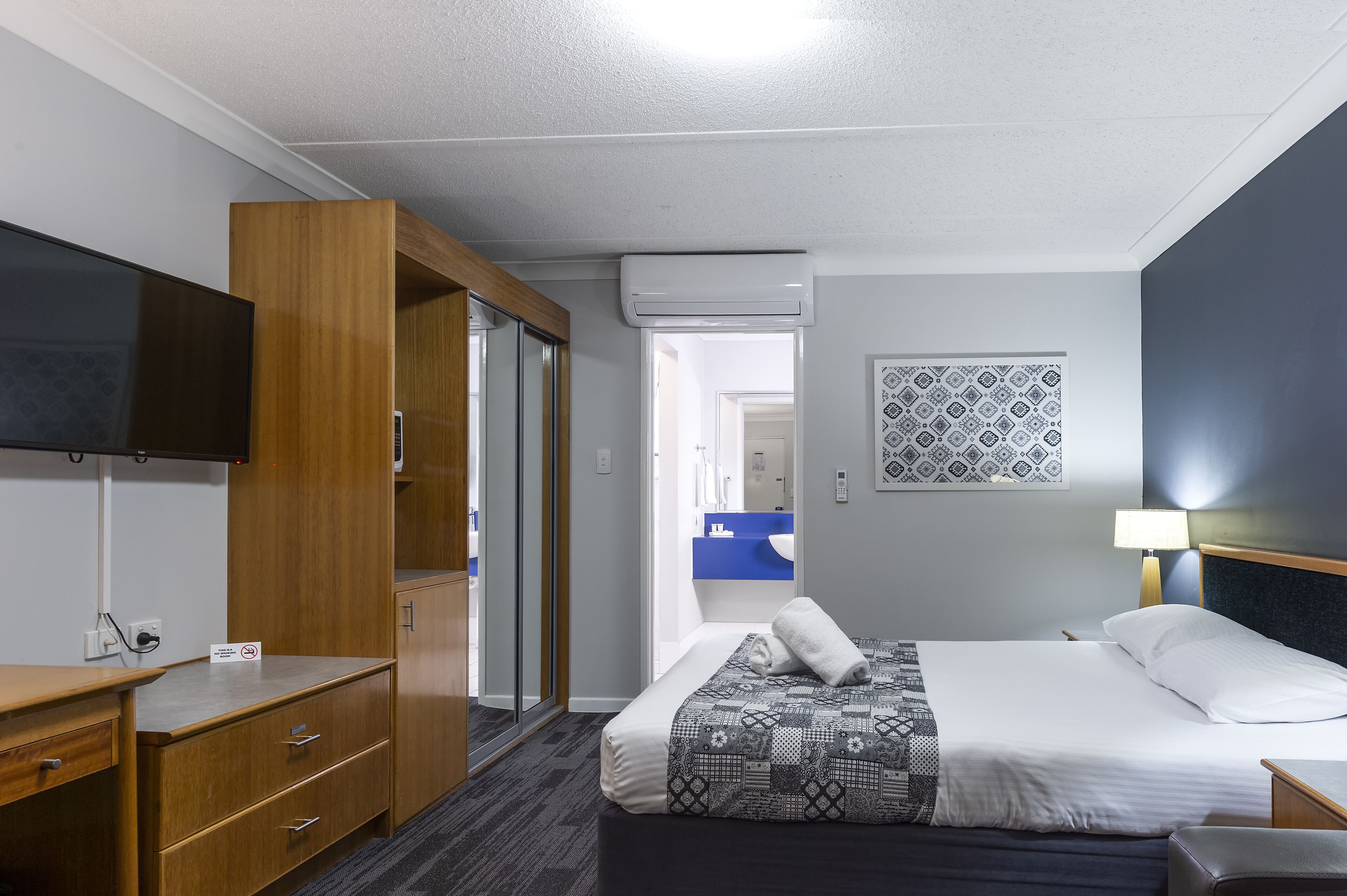 A hotel room with a bed, a desk, a wardrobe, and a television.