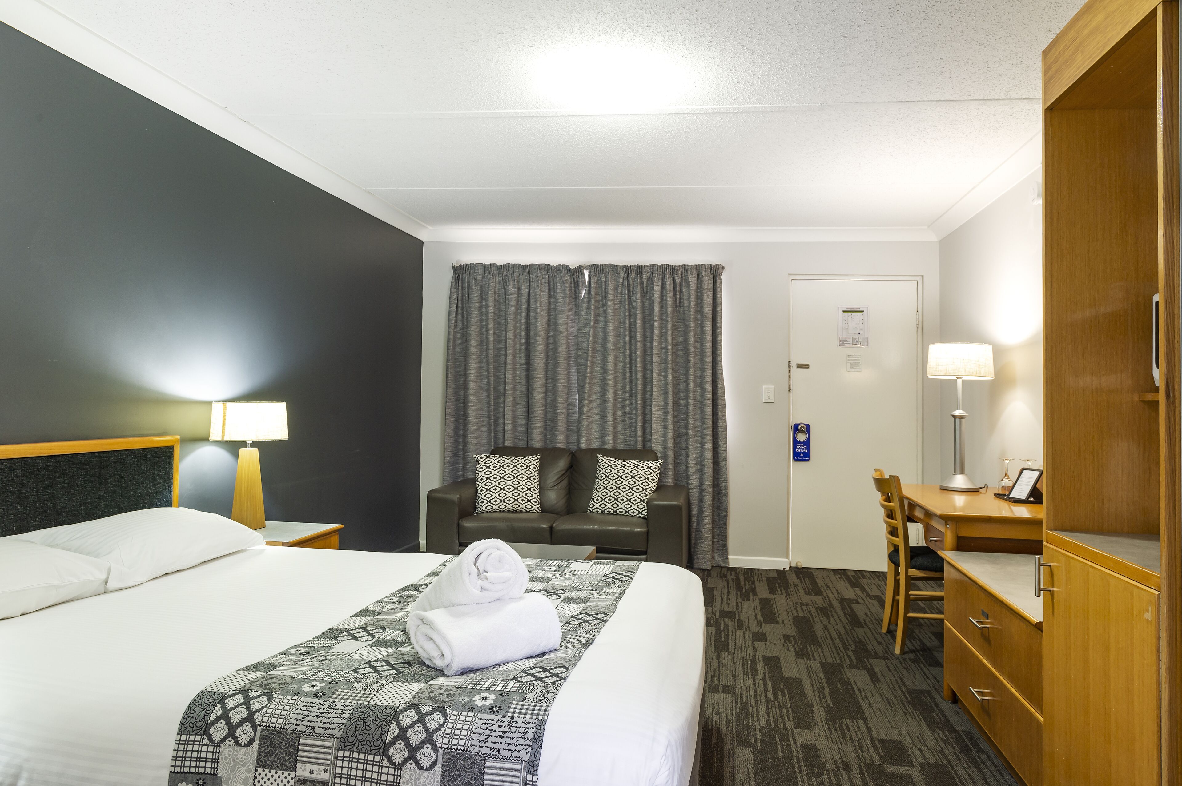 A hotel room with a bed, a desk, a chair, a wardrobe, and a curtain.