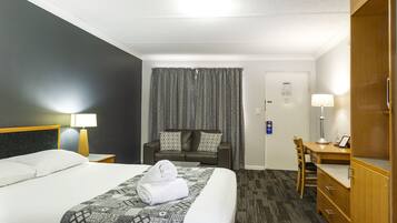 A hotel room with a bed, a desk, a chair, a wardrobe, and a curtain.