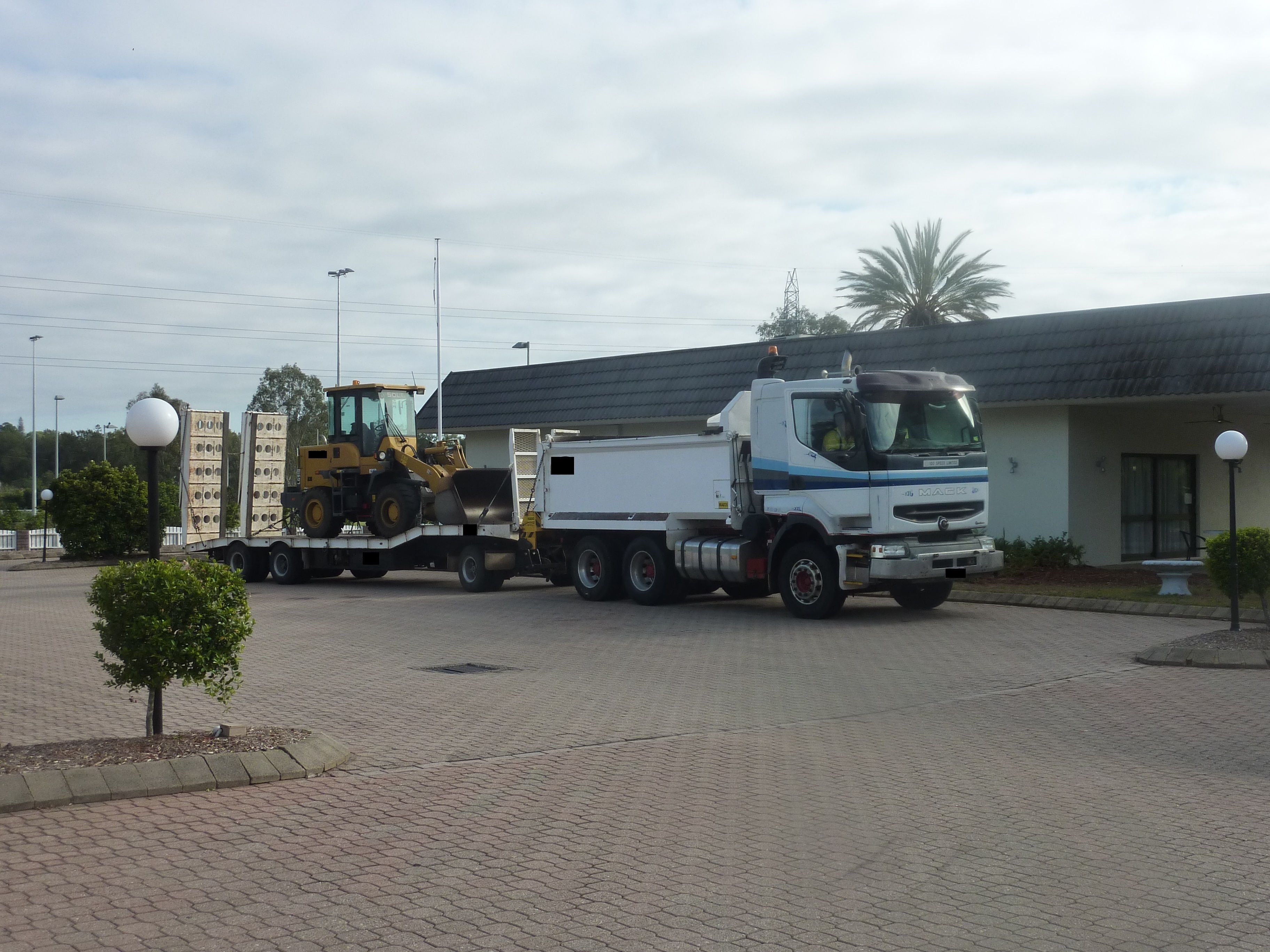 A large truck parked in front of a building with a paved driveway and a small tree.